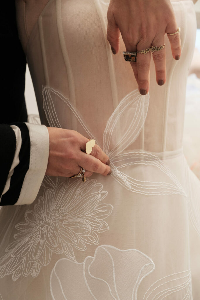 Person adjusts sheer floral dress, rings, striped shirt.