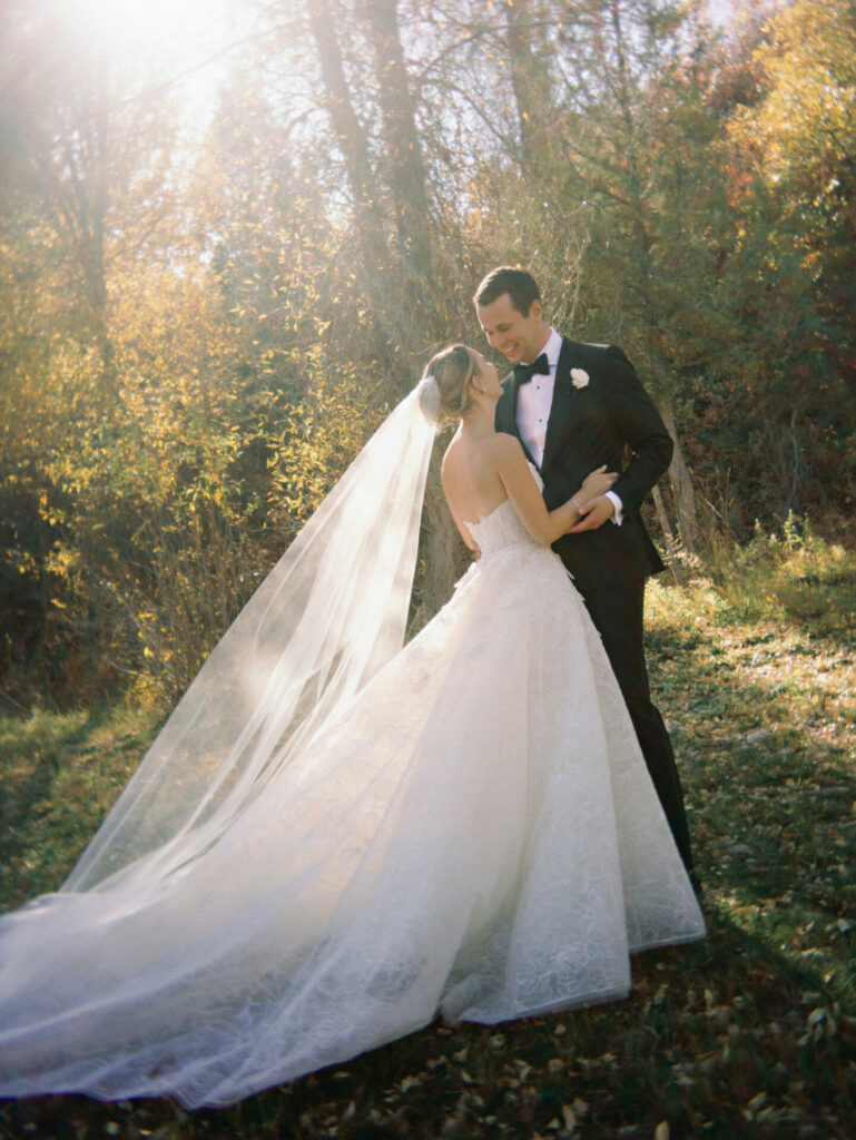 Bride and groom embrace among golden autumn trees.