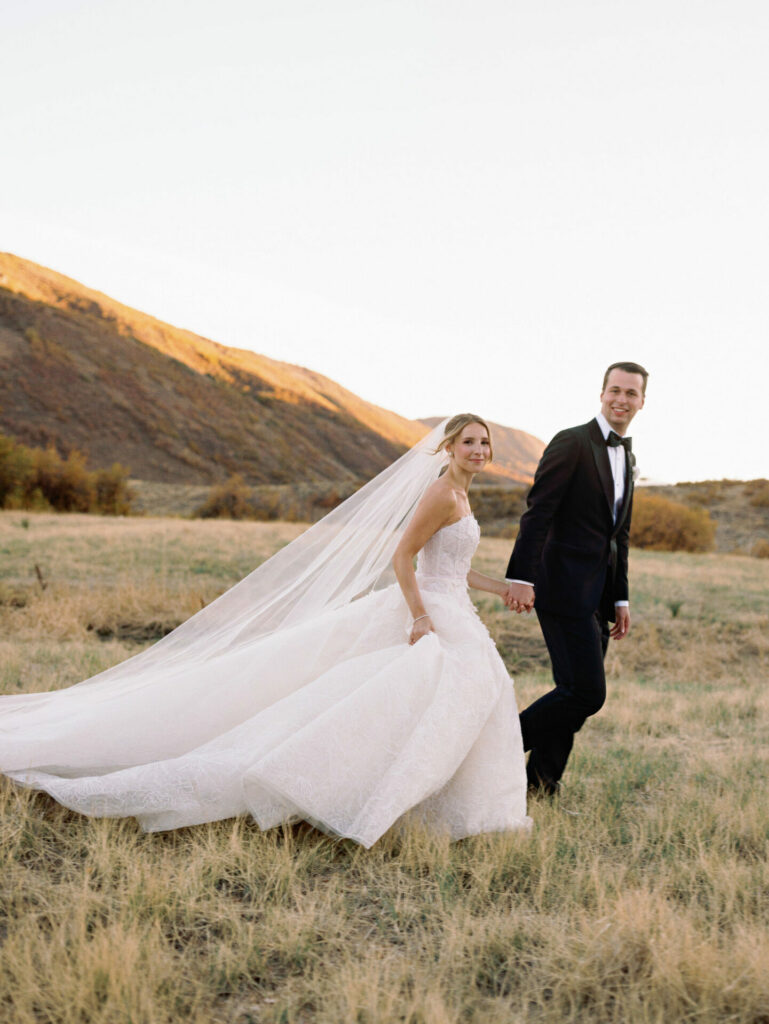 Bride and groom walk hand-in-hand at sunset.