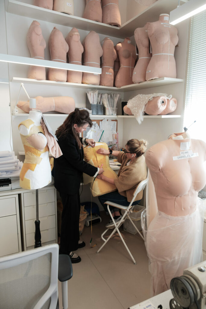 Two designers create a dress on a mannequin amid studio fabrics.