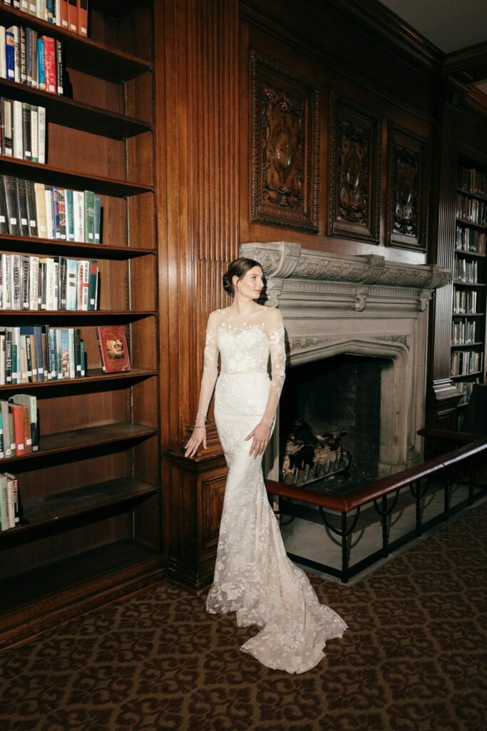 Woman in lace wedding dress by a fireplace.