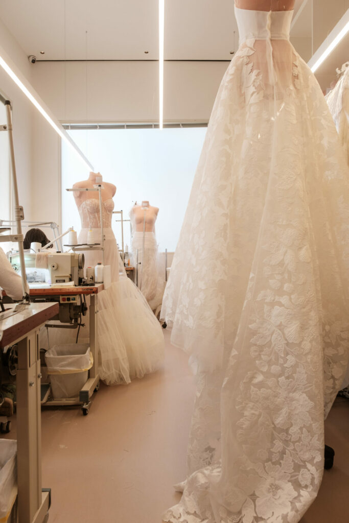 Bright atelier with sewing machines, mannequins in lace gowns.