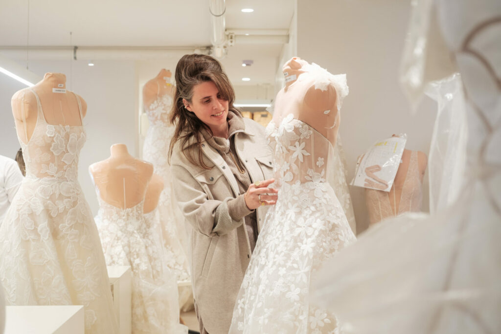 Woman inspects floral lace wedding dress in boutique.