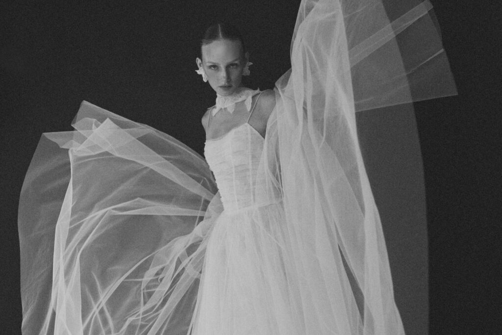 Woman in sheer white gown poses against darkness.
