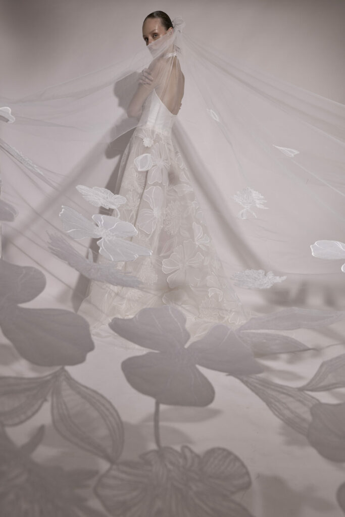 Woman models floral SS2026 gown, sheer flowered veil.