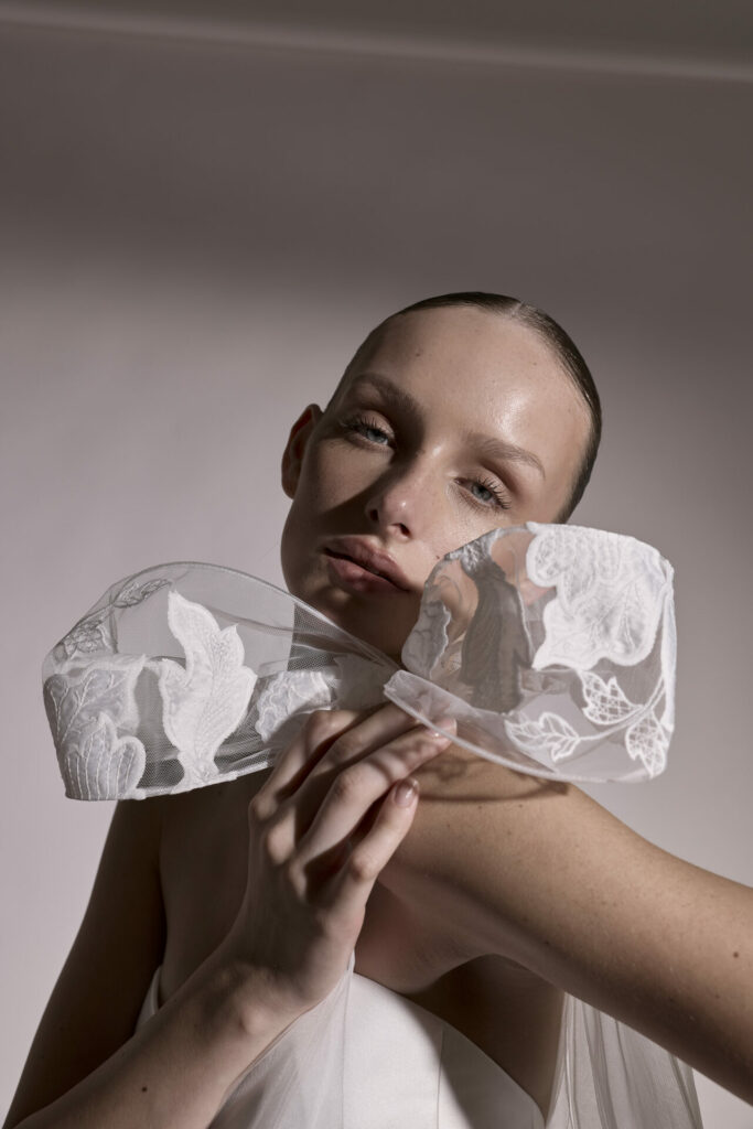 Woman with slicked-back hair holds floral sheer bow.