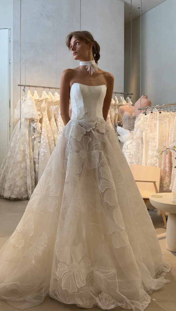 Woman in floral wedding gown at bridal boutique.