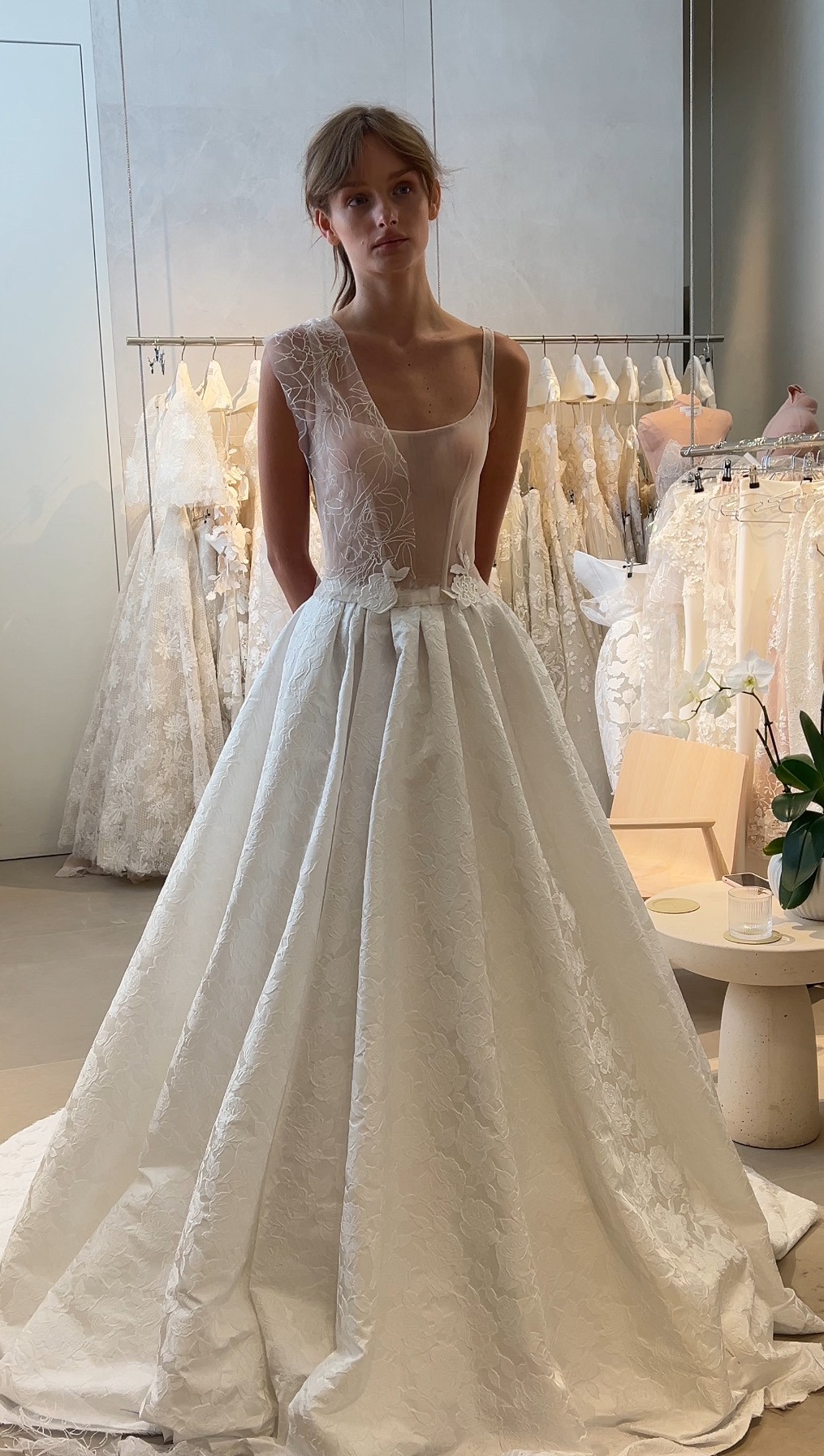 Bride in floral SS2026 dress, gowns on racks.