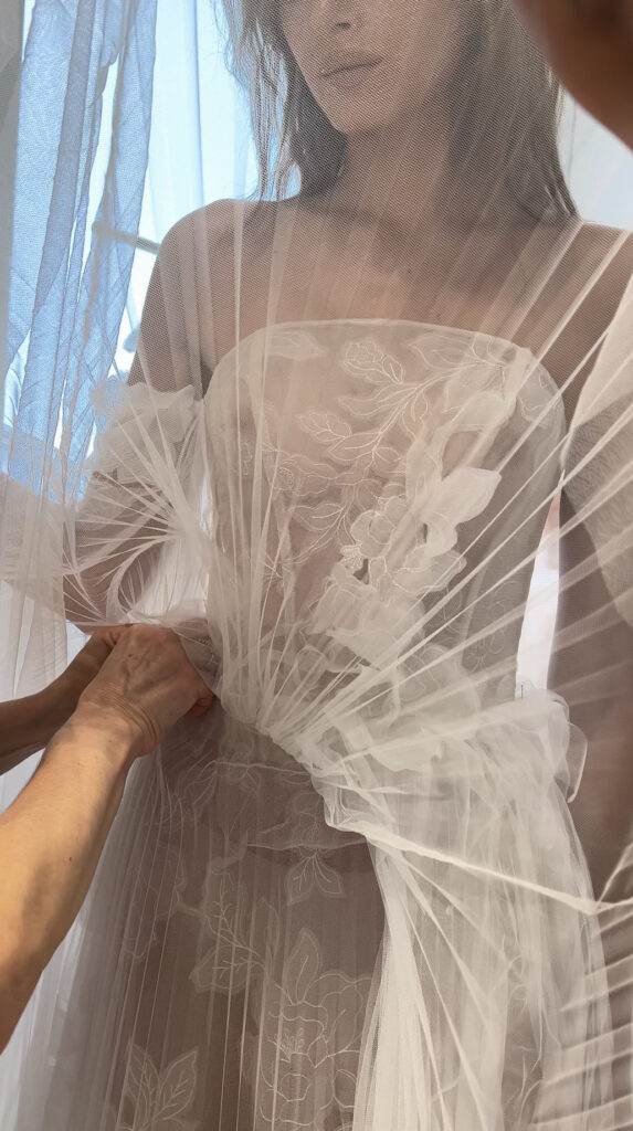 Helping adjust sheer, floral-embroidered SS2026 dress.