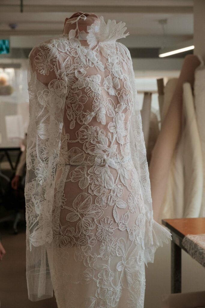 Mannequin in white lace dress, fabrics in background.