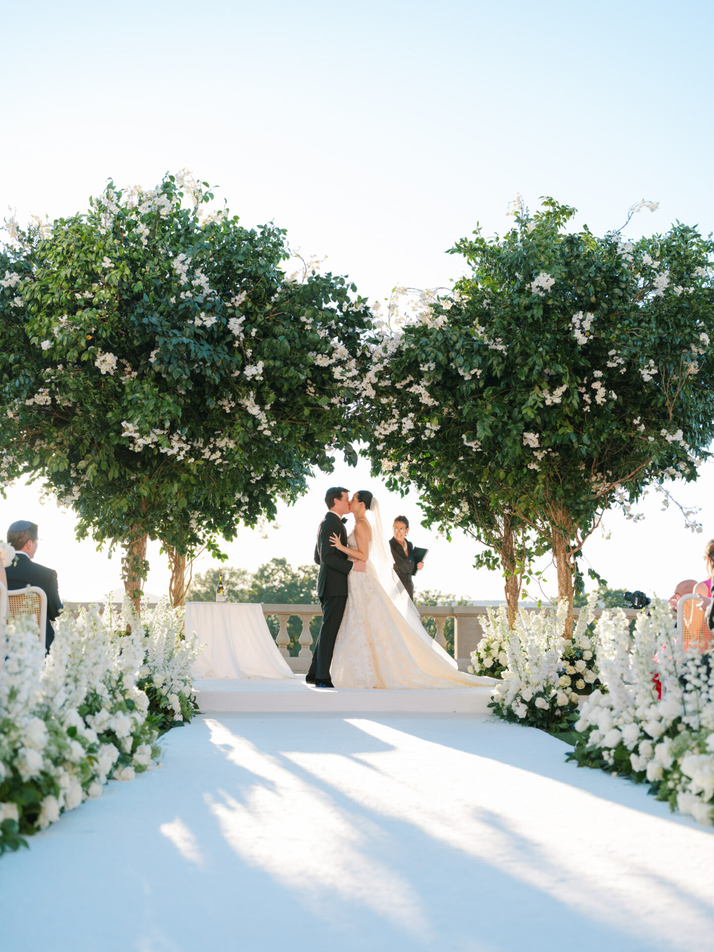 Bride and groom kiss outdoors under flowering trees.