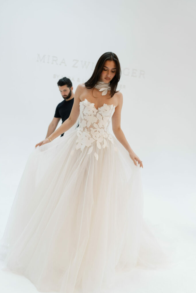 Woman in floral SS2026 wedding dress poses; man behind.