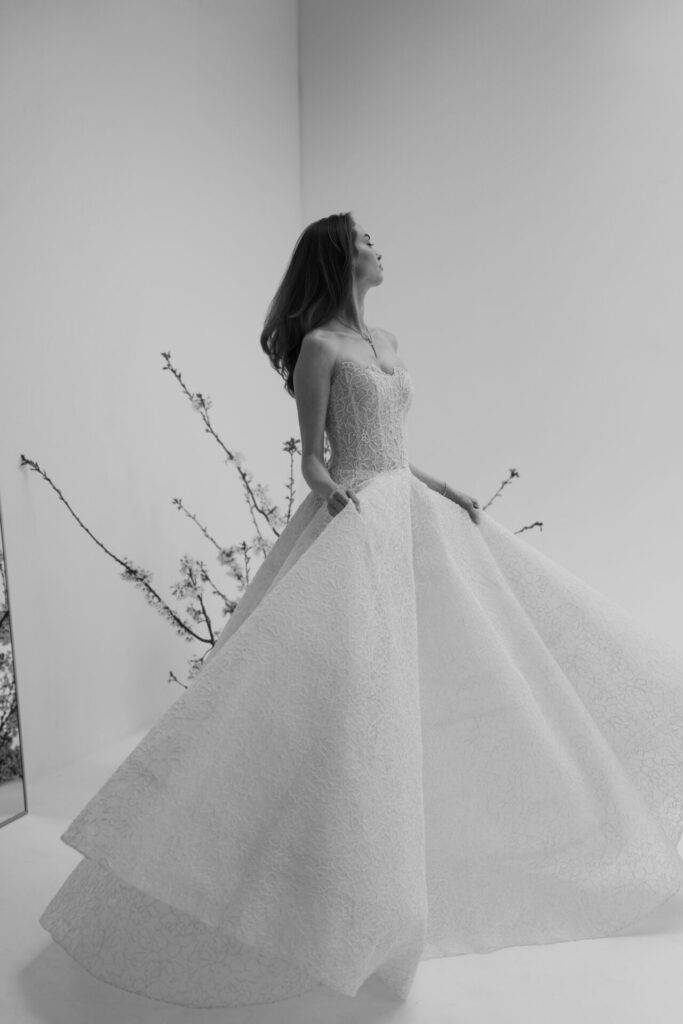 Woman in SS2026 ball gown, blossoming branches behind.