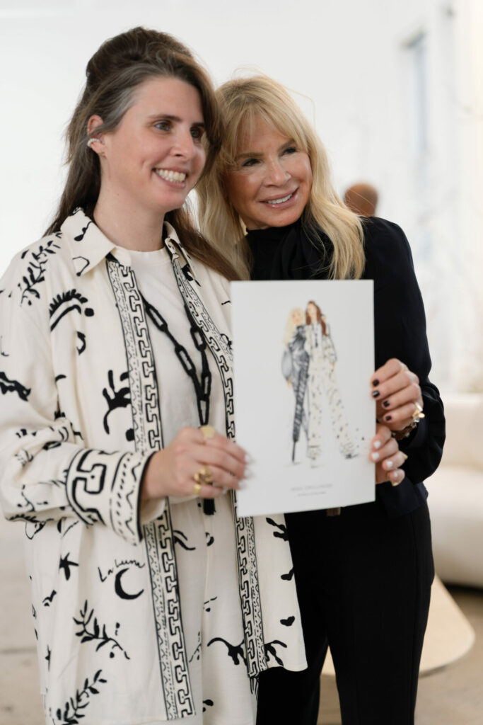 Two women posing indoors, holding a portrait together.