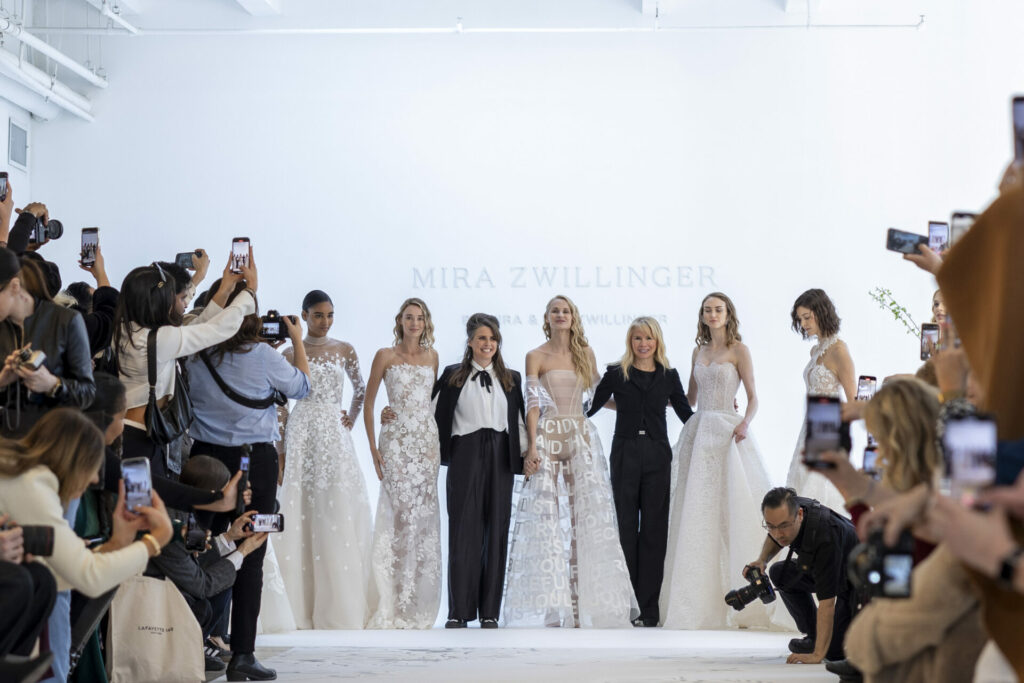Brides pose with designers on runway, Mira Zwillinger backdrop.