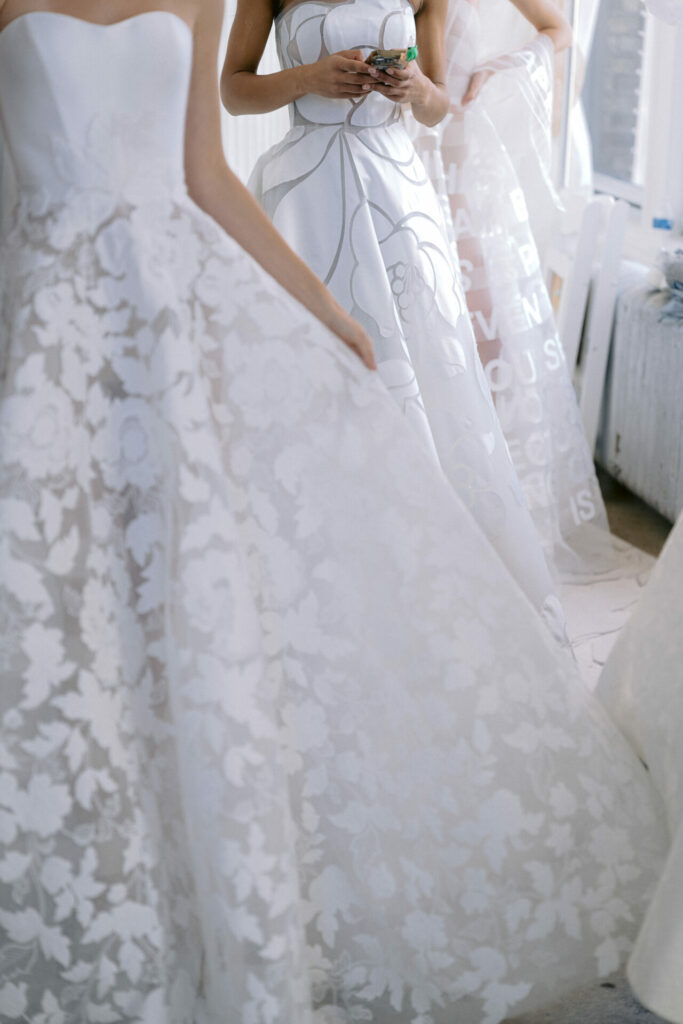 Three women in white patterned gowns stand together backstage.