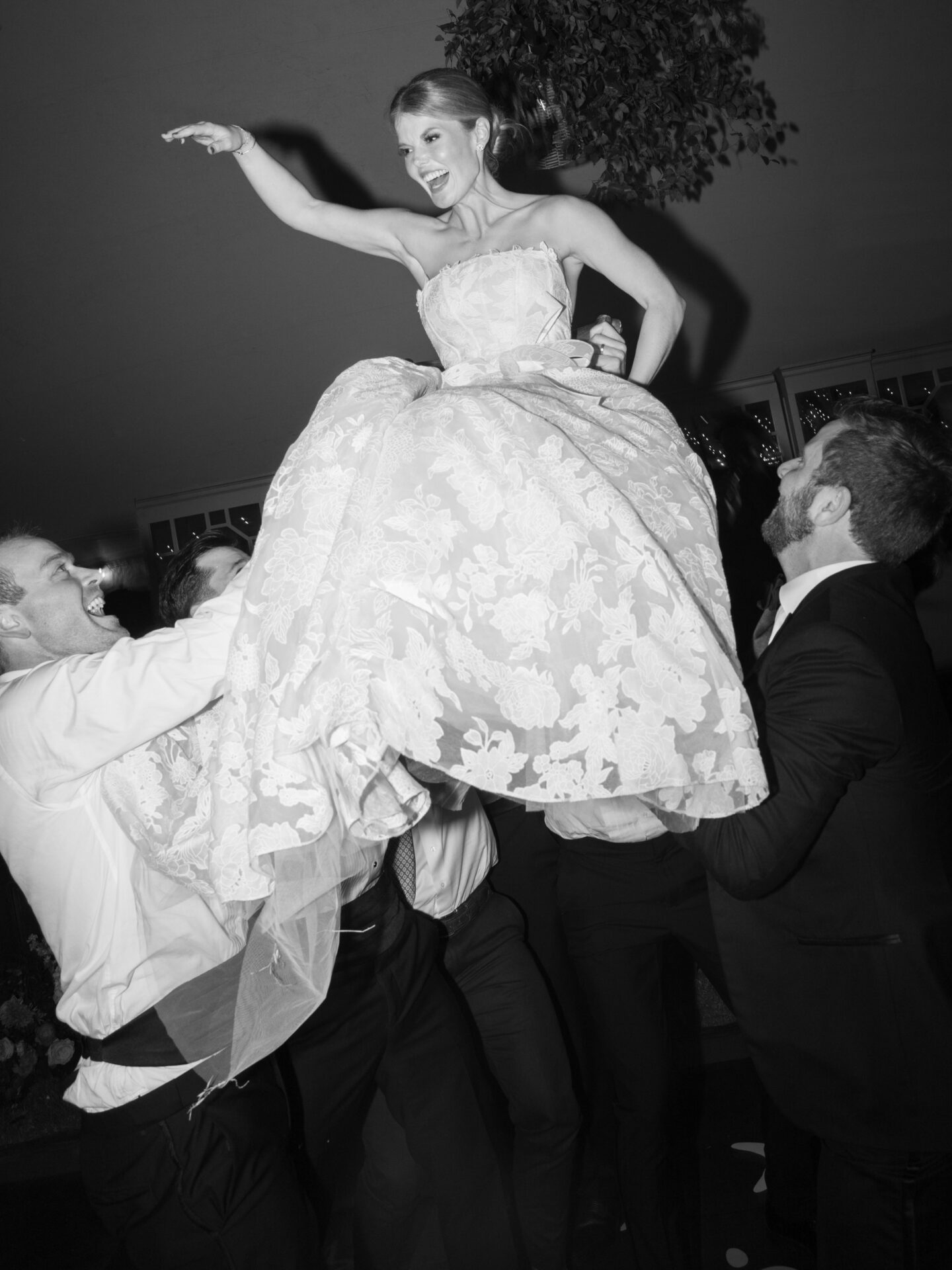 Woman in floral dress lifted at lively, festive celebration.