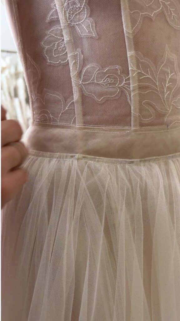 Hand holds sheer floral dress at waist, beige tulle.