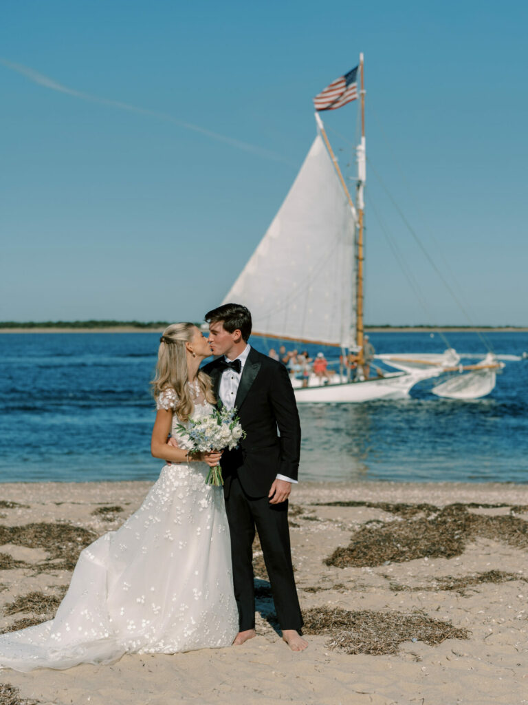 Bride in Mira Zwillinger gown embraces groom on beach.