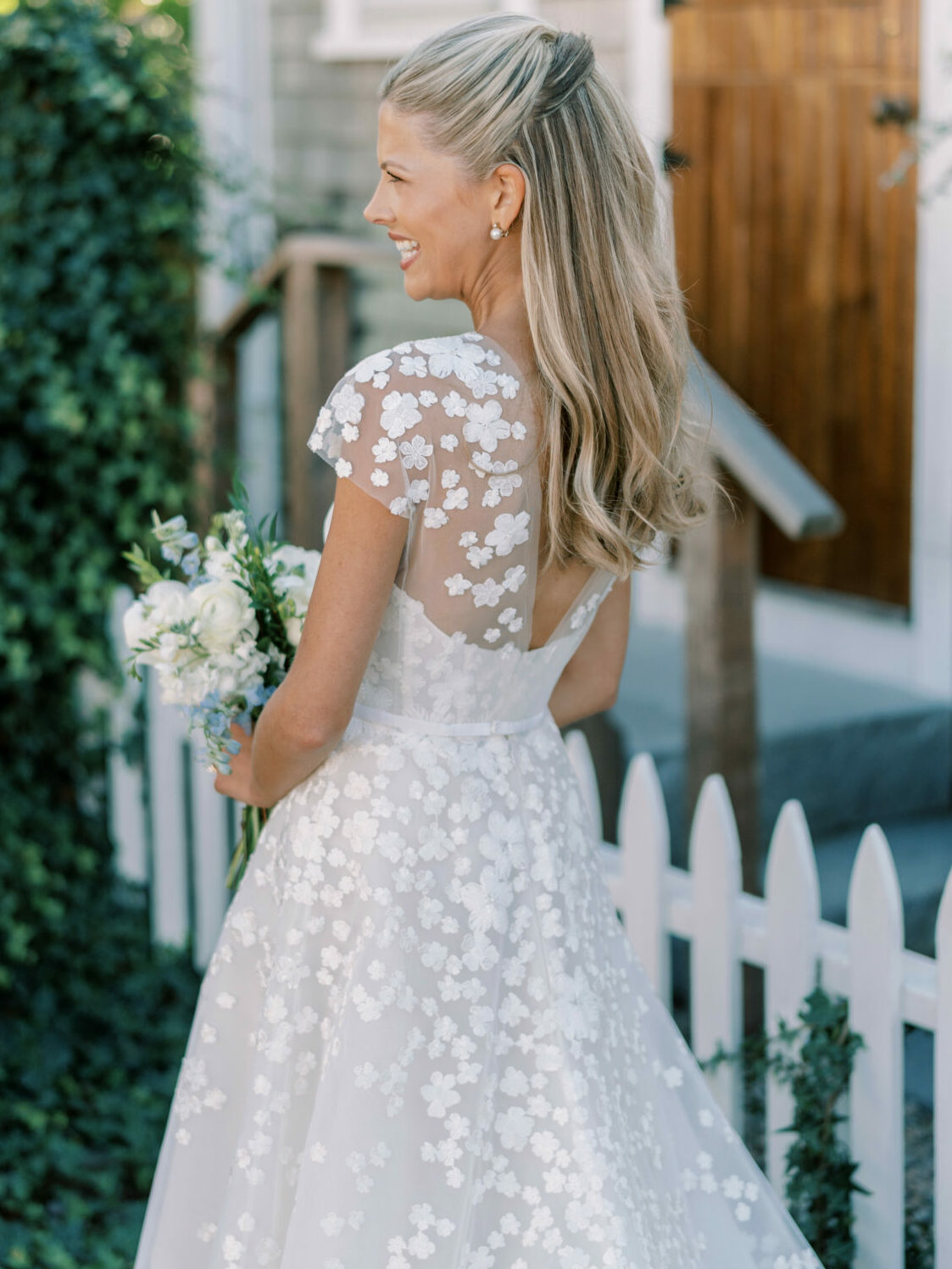 Smiling bride in couture gown by picket fence.