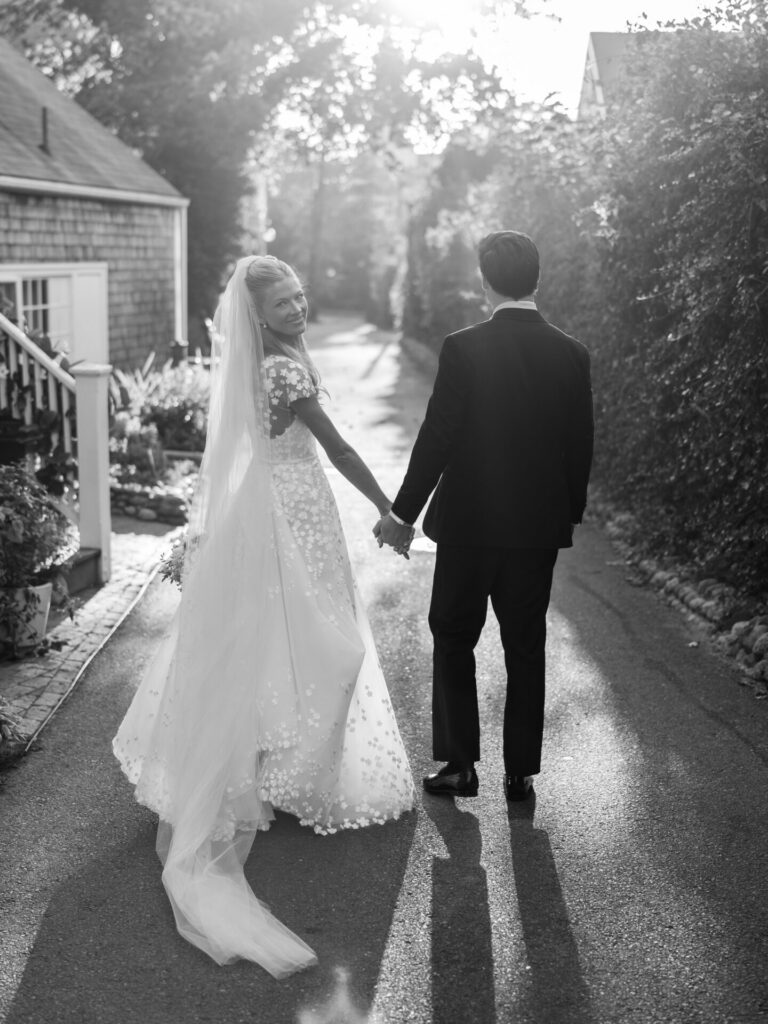 Bride in couture gown smiles, walking hand-in-hand outdoors.