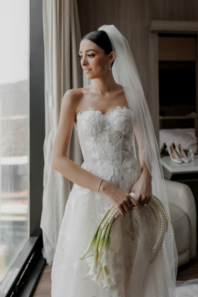 Bride in couture gown by window with lilies.