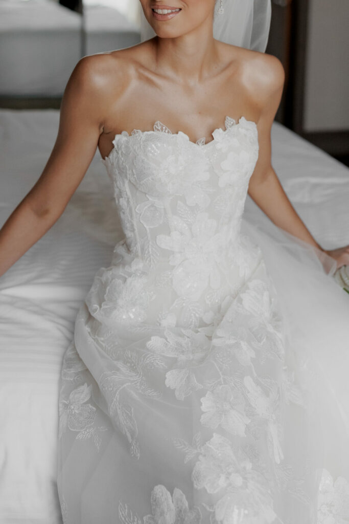 Katya Ruiz smiles on bed in strapless lace gown.