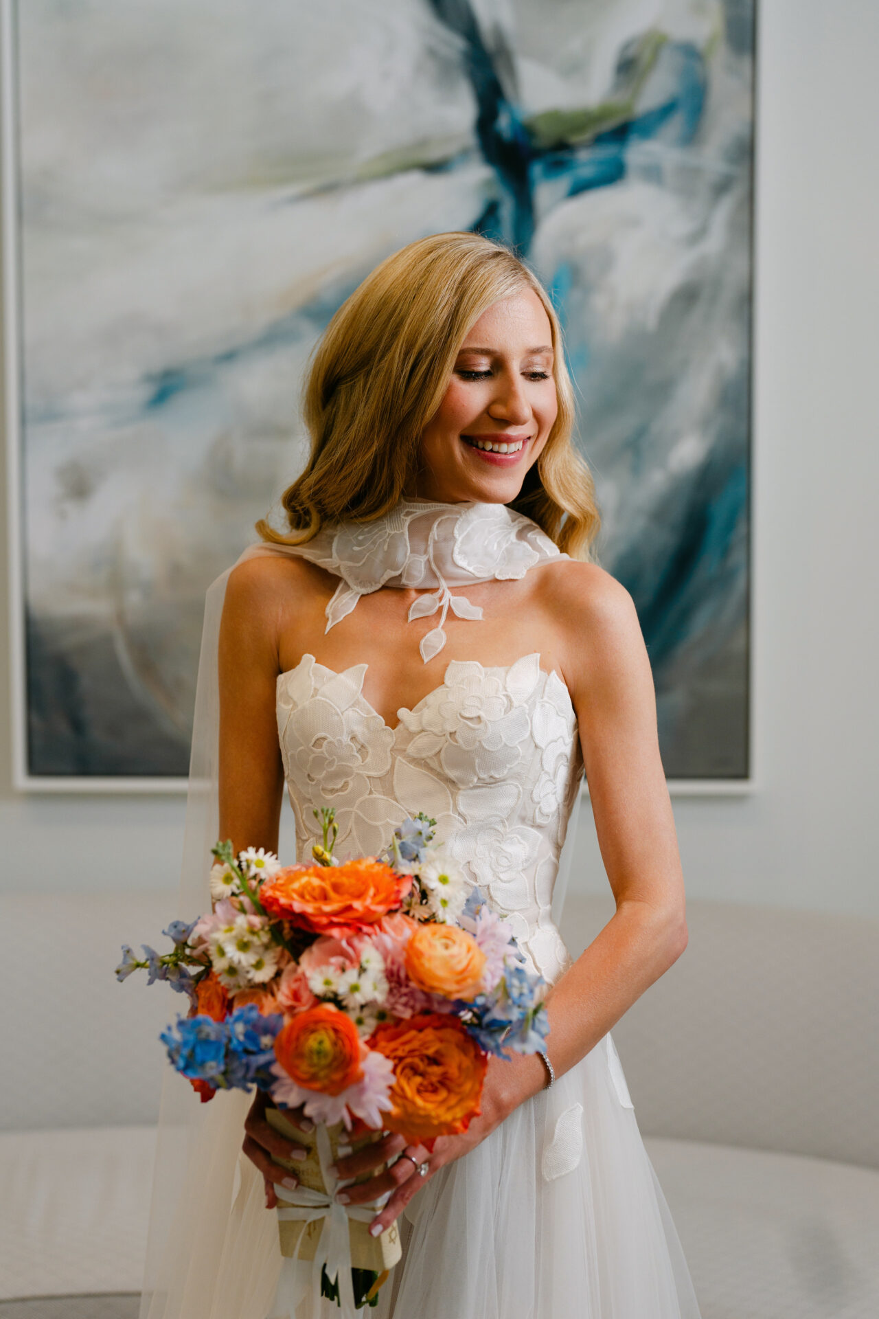 Bride with bouquet in lace dress before abstract painting.