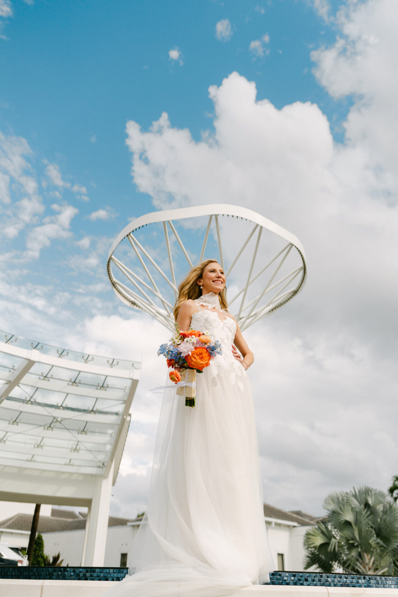 Bride with orange-blue bouquet under white canopy.