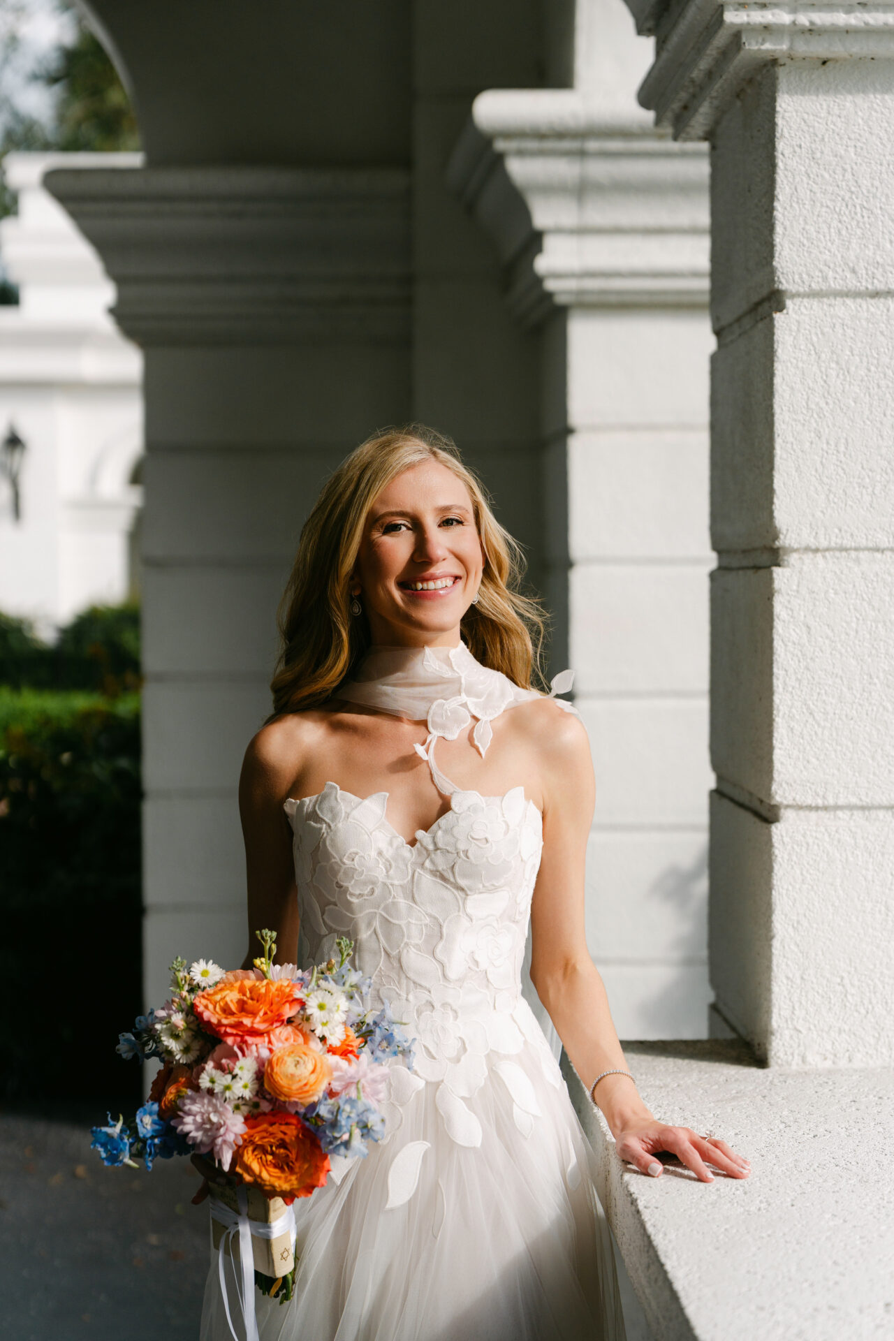 Bride in floral dress holding bright bouquet outdoors.