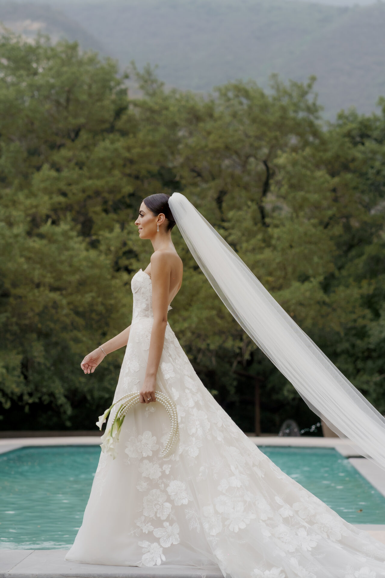 Katya Ruiz in floral lace gown by pool, mountains behind.