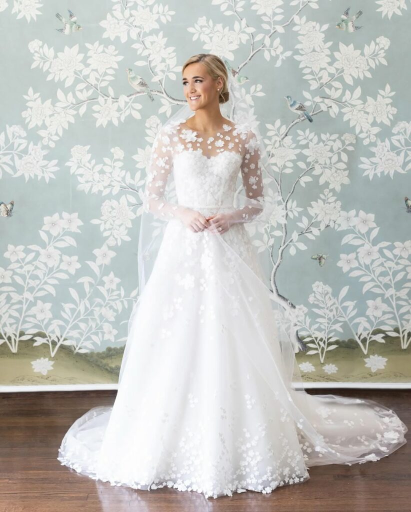 Bride in white lace gown by blue floral wall.