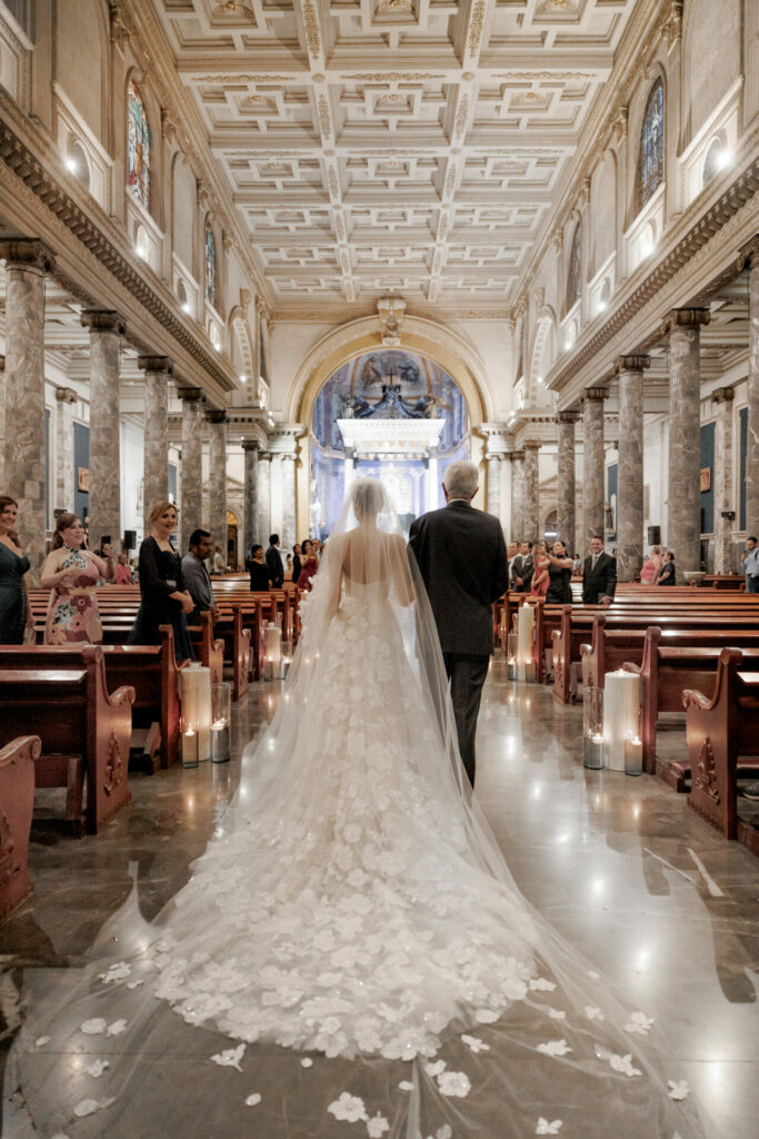 Bride in couture gown walks aisle with older man.