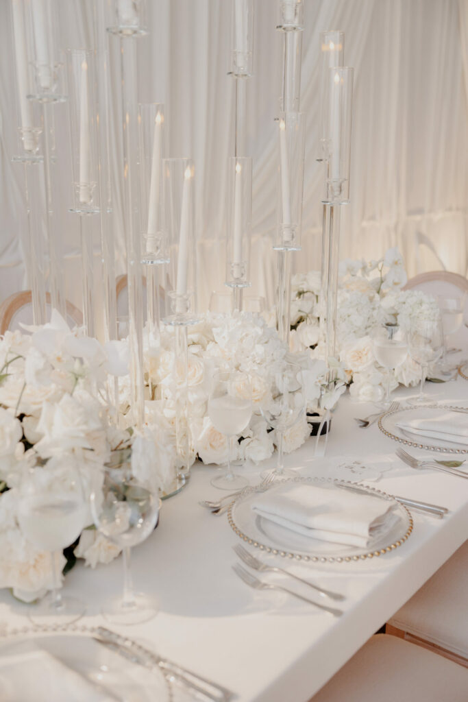 Luxury wedding table with white flowers, candles, silver plates.
