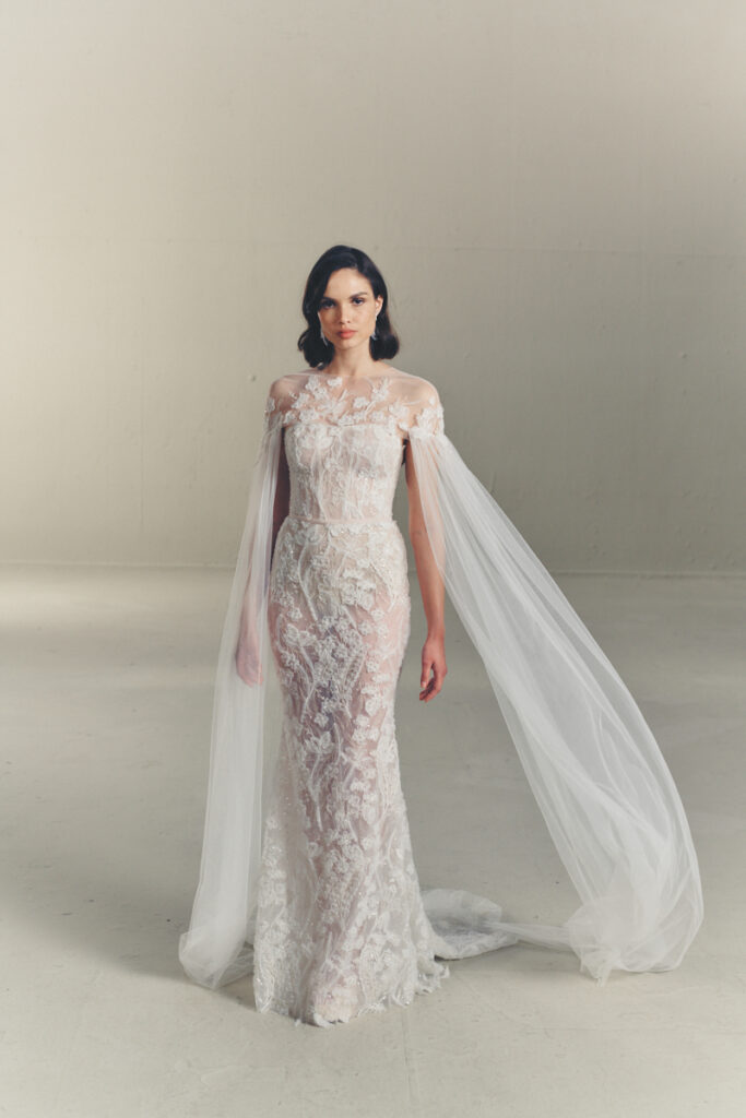Woman in sheer lace wedding gown with cape sleeves.