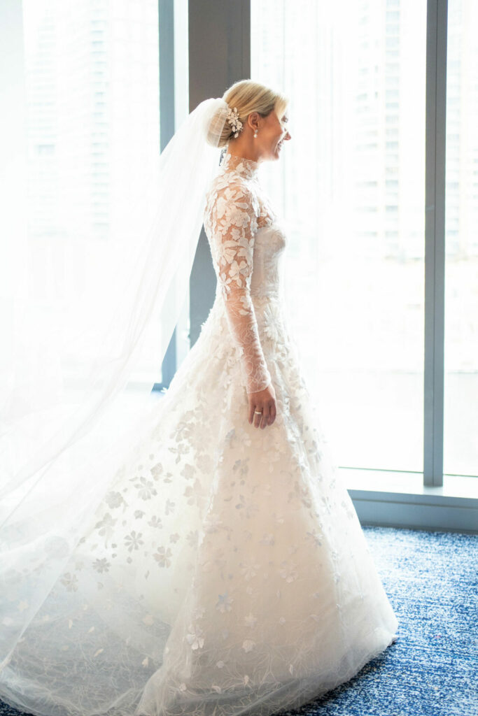 Bride in lace gown smiles by city windows.