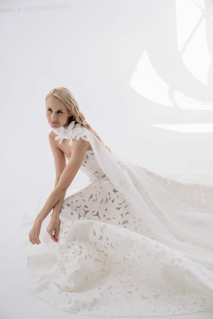 Woman in floral white gown kneels, minimal background.