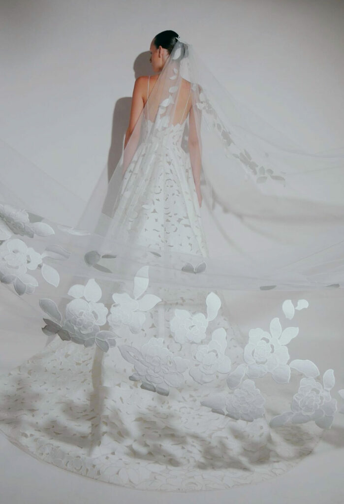 Bride in floral veil and gown faces away.