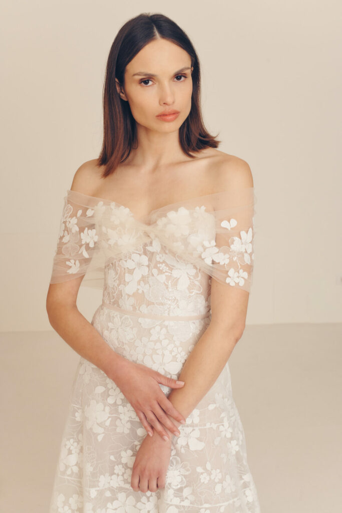 Woman in white lace dress, neutral expression.