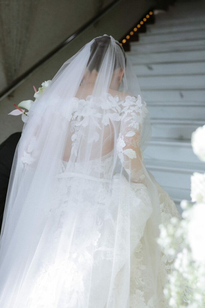 Bride in couture gown ascends stairs, bouquet in hand.