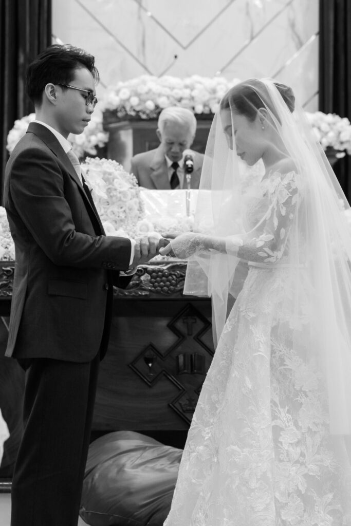 Groom puts ring on bride’s finger, black and white.