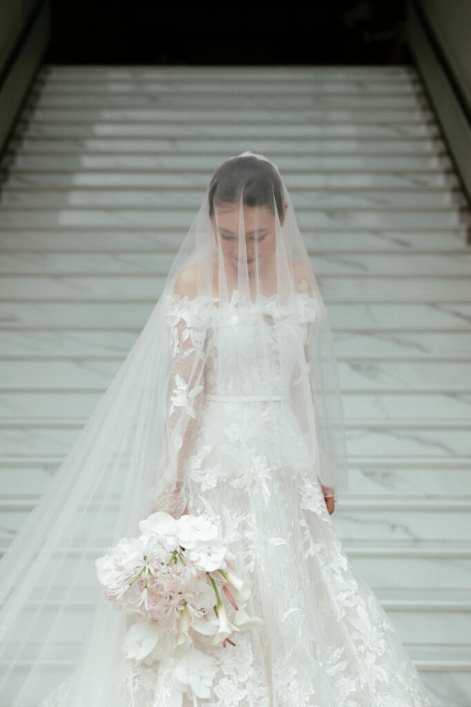 Katya Ruiz poses on marble stairs in lace gown.