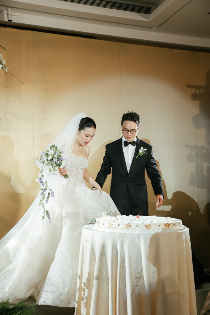 Bride and groom cutting cake, luxury gown and bouquet.