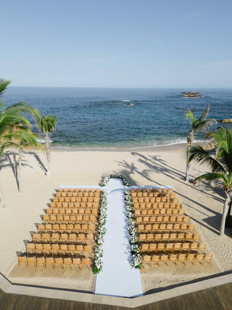 Wooden chairs on beach, aisle runner, palm trees.