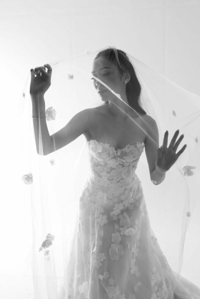 Woman in floral lace gown holding sheer flower veil.