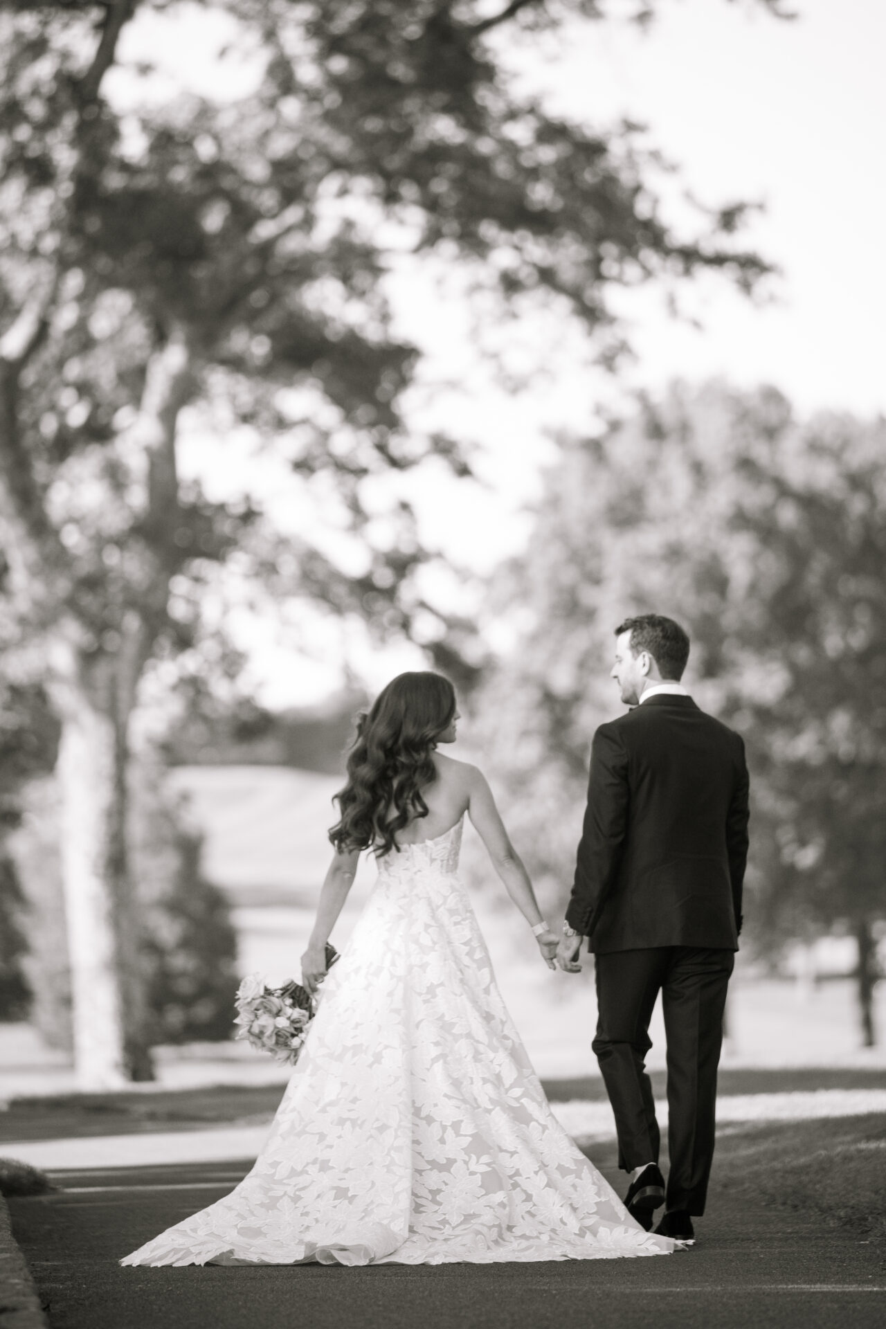 Bride and groom walk hand in hand, black and white.