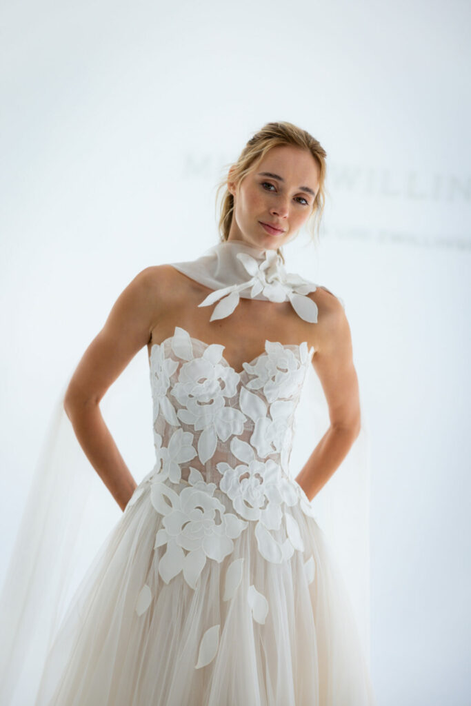 Woman in strapless floral wedding dress poses confidently.