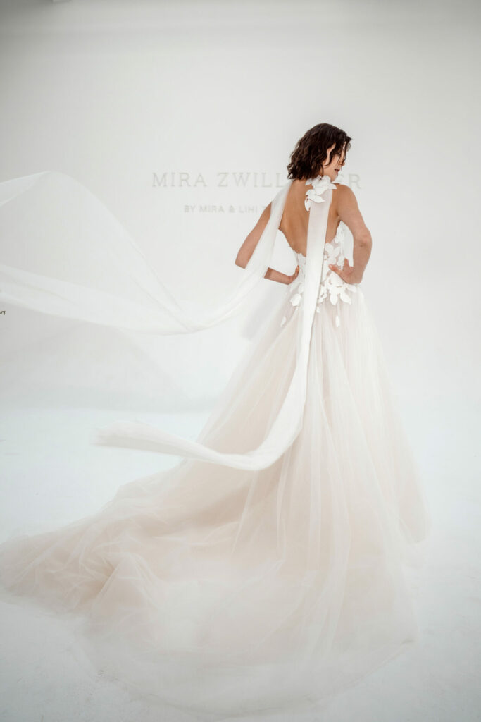 Bride in white gown with ribbons, studio background.