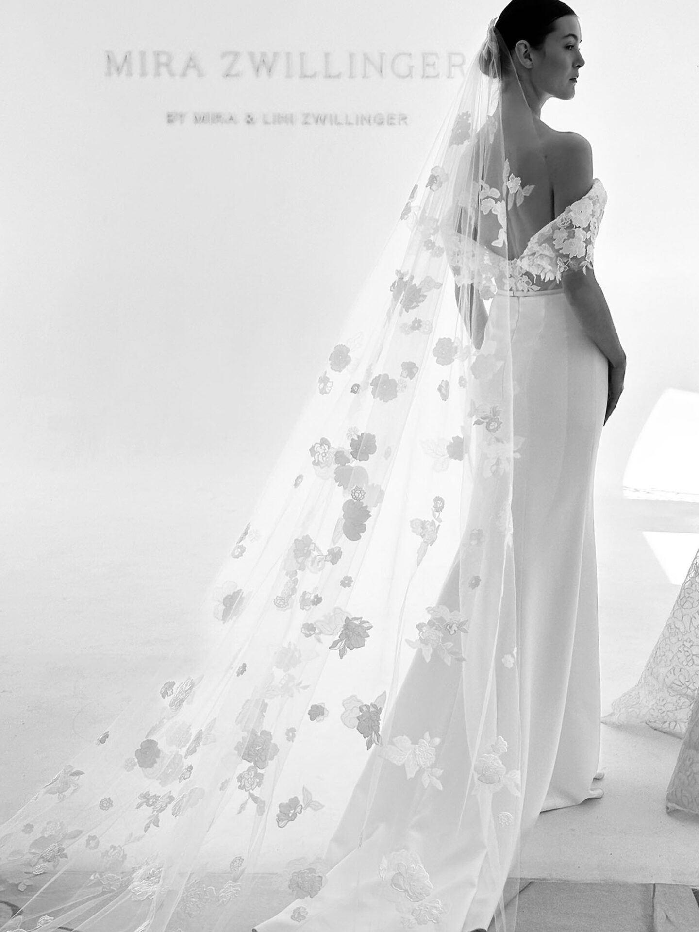 Bride in floral-veiled dress poses; bright, minimal setting.