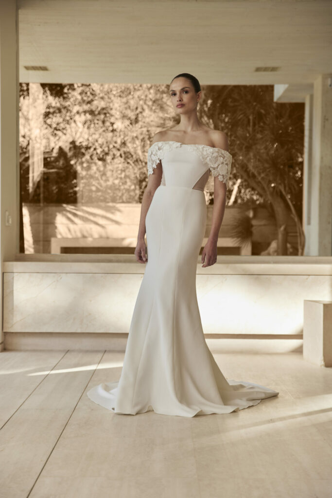 Woman in white off-shoulder lace wedding gown indoors.